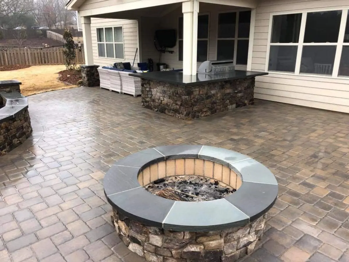 Round stone fire pit on a paver patio with a stone outdoor kitchen bar in the background