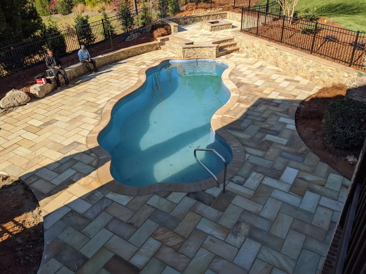 Herringbone stone pool deck surrounding a freeform pool with a raised stone fire feature